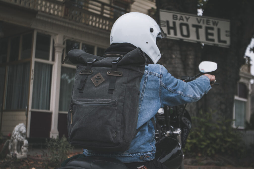 A motorcyclist with a white helmet wearing a Revelry Supply - Drifter Backpack